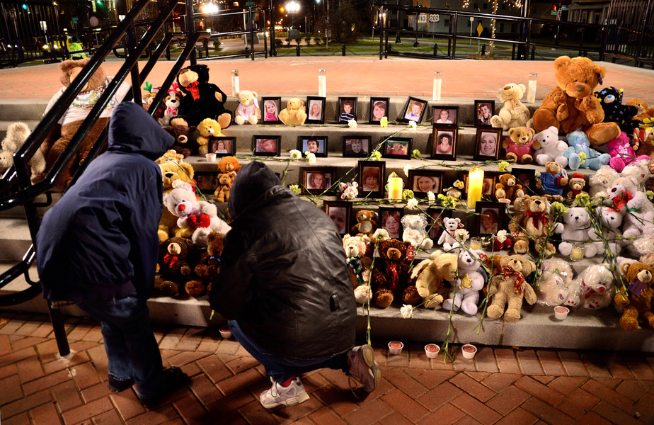 A woman and child view photos, flowers and teddy bears on steps.