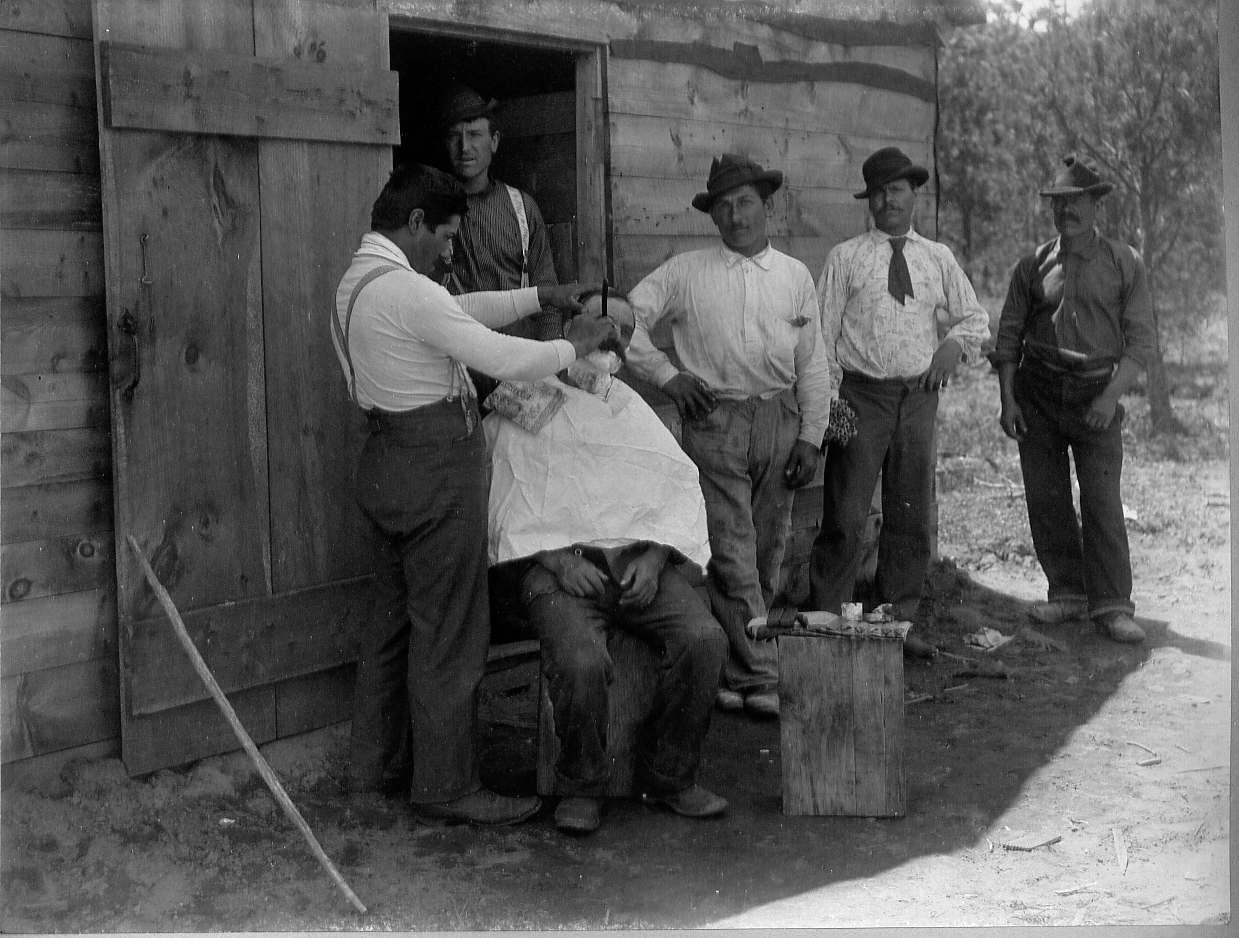 Men standing watching man shaving another man's face